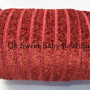 May include: A roll of red glitter elastic ribbon. The ribbon is a vibrant red color and is covered in glitter, giving it a sparkling appearance. The text "Oh Sweet Baby Boutique" is printed on the ribbon.