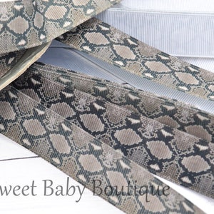 May include: Close-up of several rolls of ribbon. The ribbon features a snakeskin pattern in shades of gray, brown, and black. A white ribbed ribbon is also visible. The text "Oh Sweet Baby Boutique" is at the bottom.