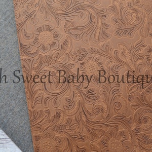 May include: A close-up of a brown faux leather fabric with an embossed floral pattern. The fabric has a textured surface and a rich brown color.