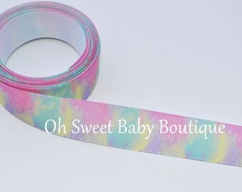 May include: A roll of pink, blue, and yellow tie-dye ribbon with white glitter. The ribbon is 1.5 inches wide and has a white backing. The text "Oh Sweet Baby Boutique" is printed on the ribbon.
