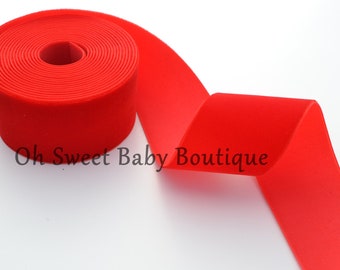 May include: A roll of bright red velvet ribbon, unspooled to reveal its soft texture. The ribbon is tightly wound, with a smooth, matte finish. The text "Oh Sweet Baby Boutique" is visible on the ribbon.