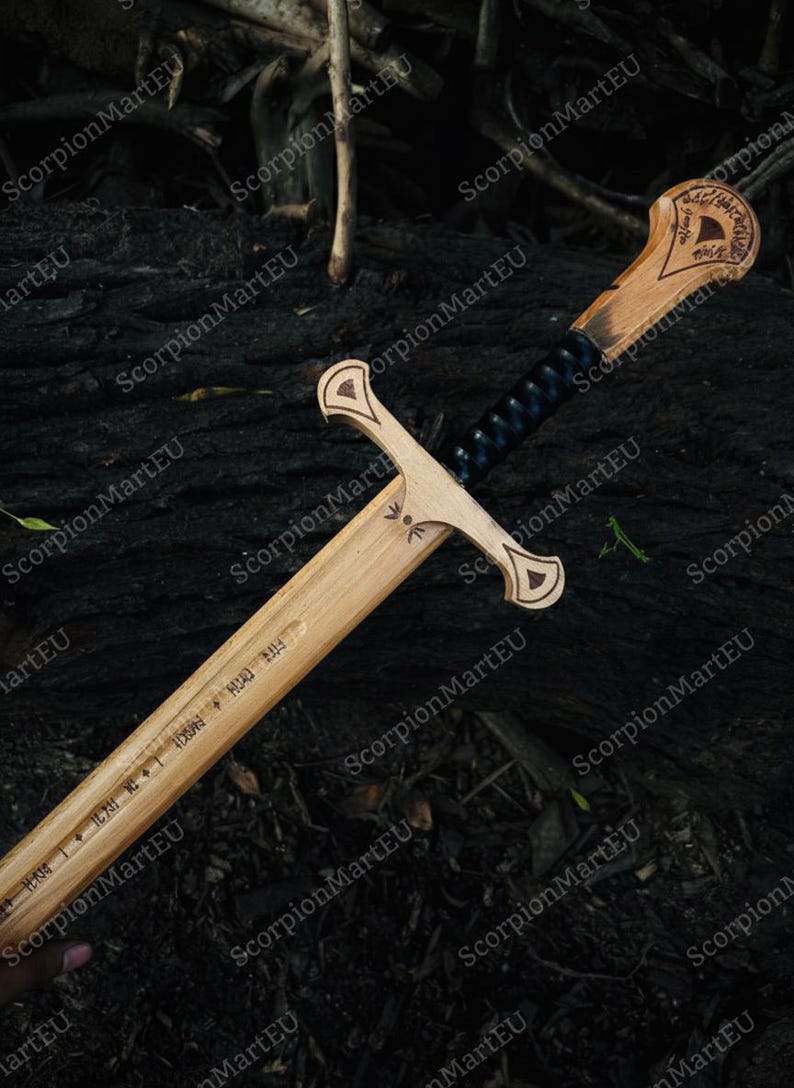 May include: A wooden sword with a light brown blade and handle, featuring intricate carvings and a dark blue wrapped grip. The blade has engraved text. The sword is displayed against a dark, textured background.