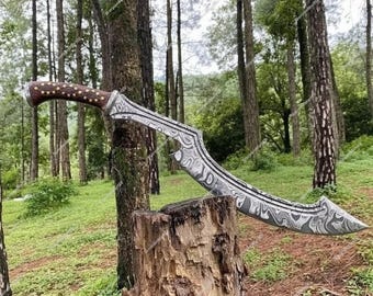 May include: A curved, silver-colored sword with a patterned blade and a wooden handle with a dotted design. The sword is displayed on a tree stump in a forest setting.