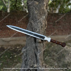 Puede incluir: Una espada larga y plateada con una hoja oscura y texturizada y un mango de madera. El mango tiene un agarre marrón oscuro y un pomo decorativo. La espada está apoyada contra un tronco de árbol.