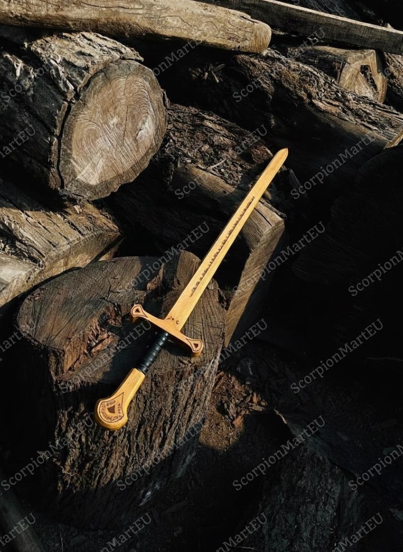 May include: A wooden sword with a light brown blade and a black handle, resting on a pile of cut logs. The sword features a crossguard and a detailed hilt design. The blade has etched text.