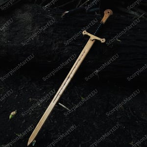 May include: A wooden sword with a crossguard and a detailed handle. The blade has a carved design along its length. The sword is set against a dark, natural background, suggesting an outdoor setting. The overall aesthetic is reminiscent of fantasy weaponry.