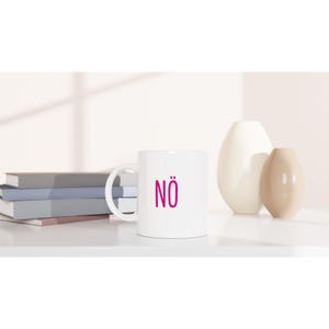 Può includere: Una tazza di ceramica bianca con manico nero e la scritta "But First, Coffee" in nero, in grassetto. La tazza è su una superficie bianca. La tazza sembra contenere circa 355 ml.