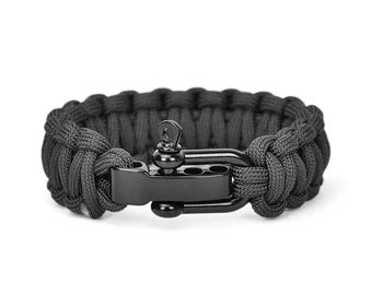 May include: Black paracord bracelet with a black metal clasp. The bracelet is made of tightly woven black cord, with a secure, industrial-style clasp. The clasp has a hook and a bar that interlocks to fasten the bracelet.