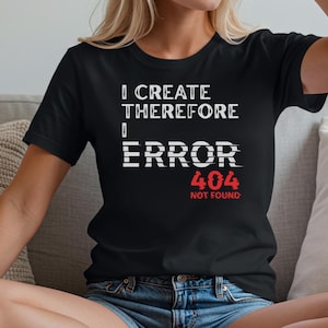 以下が含まれることがあります： 「I CREATE THEREFORE I ERROR 404 NOT FOUND」の文字が白と赤でプリントされた黒いTシャツ。デザインはグリッチエフェクト。Tシャツはクルーネックで半袖です。