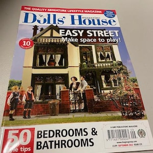 Könnte beinhalten: Ein Magazin-Cover für das Magazin Dolls' House, das eine farbenfrohe Illustration eines Puppenhauses mit einer roten Backsteinfassade und einer grünen Haustür zeigt. Der Text auf dem Magazin-Cover lautet "Easy Street Make space to play!" und "50 Bedrooms & Bathrooms".
