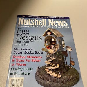 Op de afbeelding: Voorpagina van het Nutshell News magazine met een miniatuur eivormig huis met een houten trap en een hek. De titel van het magazine is "Nutshell News" en het hoofdartikel is "Egg Designs That Aren't to Dye For".