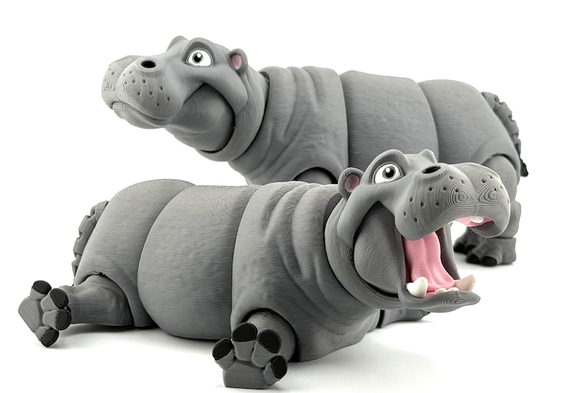 K&ouml;nnte beinhalten: Zwei graue, bewegliche Nilpferd-Figuren. Ein Nilpferd liegt mit offenem Maul, das rosa Innere und wei&szlig;e Z&auml;hne zeigt. Das andere Nilpferd ist im Hintergrund und blickt nach oben. Die Nilpferde haben eine strukturierte Oberfl&auml;che auf wei&szlig;em Hintergrund.