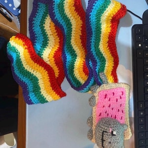 Peut inclure: Un design artisanal au crochet représentant Nyan Cat et un arc-en-ciel. Nyan Cat est une Pop-Tart rose avec un visage de chat gris et une traînée arc-en-ciel multicolore.