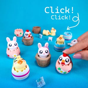 Könnte beinhalten: Eine Sammlung farbenfroher, miniaturisierter Tierfiguren, darunter Hasen, Küken und Enten, einige in eiförmigen Behältern und Körben. Der Text "Click! Click!" wird auf blauem Hintergrund angezeigt.