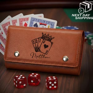 May include: A brown leather card holder with a crown and ace card design, personalized with a name. Three red dice with white dots are in front of the holder, and playing cards are visible. The holder is secured with two silver snaps.
