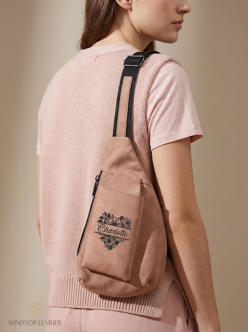 May include: A dusty rose sling bag with a black strap and zipper. The bag features a floral heart design with the name "Charlotte" printed in black. The bag is made of suede-like material.