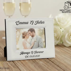 May include: A white leather picture frame with the names "Emma & John" at the top and "Always & Forever Est. 09.23.2025" at the bottom. The frame holds a photo of a couple. The Windsor Leather logo is at the bottom.