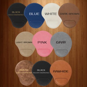 K&ouml;nnte beinhalten: Eine Auswahl an ergonomischen Mauspads in verschiedenen Farben: Schwarz, Blau, Wei&szlig;, Dunkelbraun, Hellbraun, Pink, Grau, Rustikal und Rohhaut. Jedes Pad hat eine Handballenauflage und ist mit seiner Farbe beschriftet. Die schwarzen und rustikalen Pads haben eine Goldgravur.