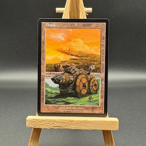 May include: A Magic: The Gathering card titled "Plains" displayed on a small wooden easel. The card features a landscape illustration with a sunset sky, a mechanical vehicle, and the text "Land".