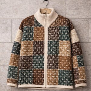 May include: A zip-up sweater with a patchwork design. The sweater has a cream-coloured collar and zip, with a pattern of squares in shades of brown, green, and cream. The sweater is hanging on a hanger.