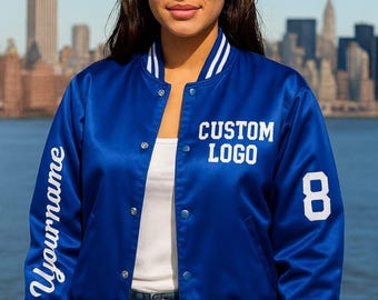 May include: A royal blue satin bomber jacket with white accents on the collar, cuffs, and hem. The jacket features the text "Yourname" on the left sleeve and "CUSTOM LOGO" and the number "8" on the front.