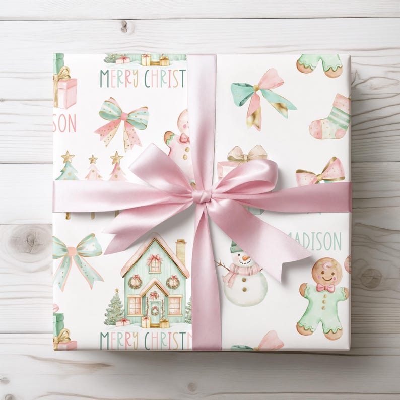 Holiday gift wrap with pastel bows, trees, and gingerbread cookies in pink and mint, shown mid-wrap with scissors and ribbon