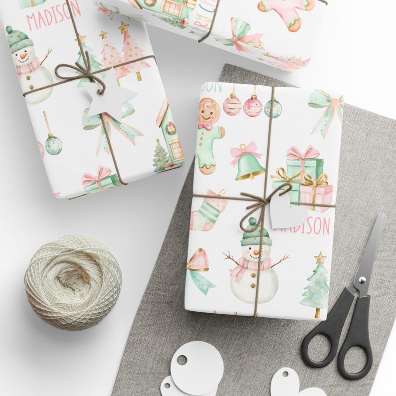 Holiday gift wrap with pastel bows, trees, and gingerbread cookies in pink and mint, shown mid-wrap with scissors and ribbon
