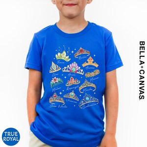 A young boy wearing a blue t-shirt with a graphic design of various crowns and tiaras.