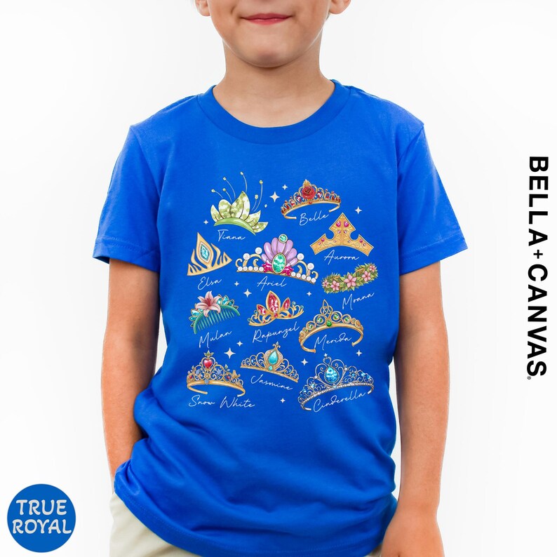 A young boy wearing a blue t-shirt with a graphic design of various crowns and tiaras.