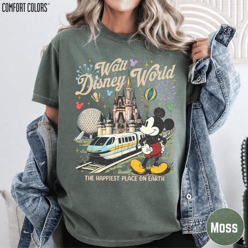 A person wearing a green t-shirt with a Disney World graphic and text, including Mickey Mouse and a train, along with the text "The happiest place on earth".