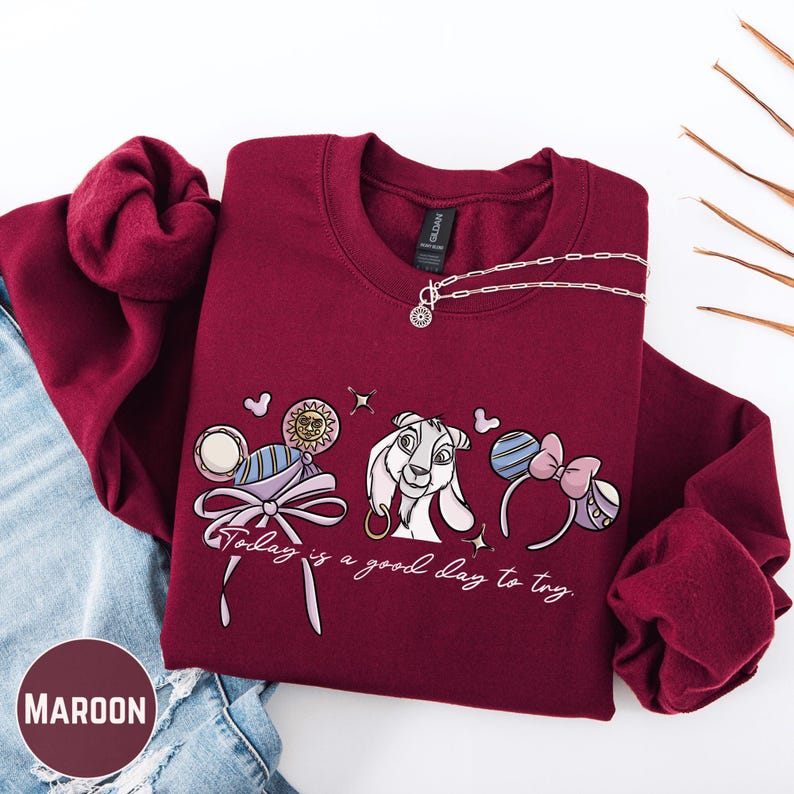 A maroon sweatshirt with a graphic design featuring a cartoon rabbit and the text "Today is a good day to try" is displayed on a white background.