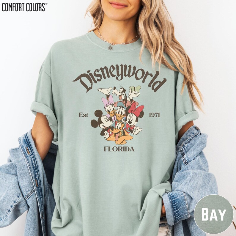 A woman wearing a green t-shirt with a Disney World logo and text, along with a denim jacket.