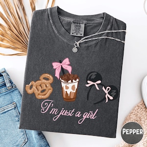 a gray t-shirt with a graphic design of a cup of coffee, a pretzel, and a pair of earrings, along with the text "I'm just a girl".