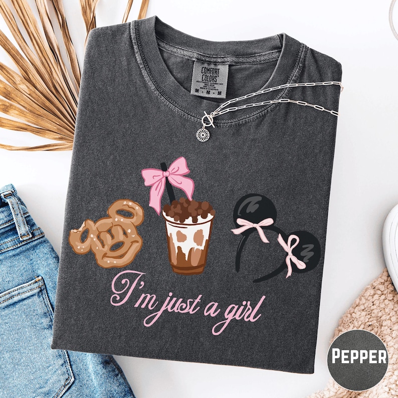 a gray t-shirt with a graphic design of a cup of coffee, a pretzel, and a pair of earrings, along with the text "I'm just a girl".