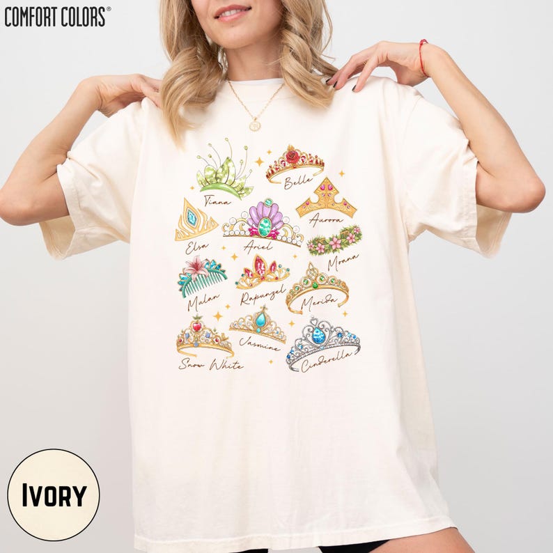 A woman wearing a white t-shirt with a graphic design of various crowns and tiaras printed on it.
