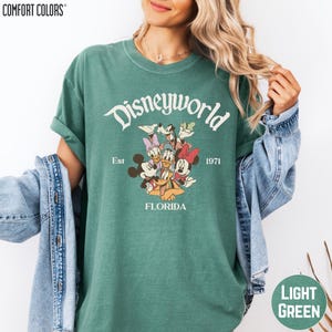 A woman wearing a green t-shirt with a Disney World logo and text, along with a denim jacket.