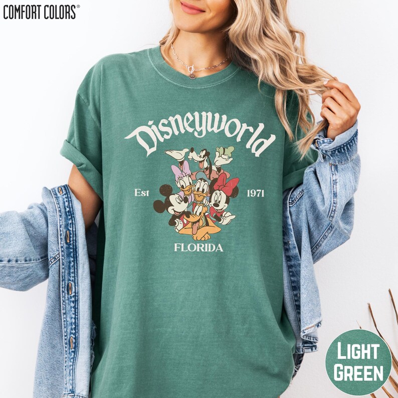 A woman wearing a green t-shirt with a Disney World logo and text, along with a denim jacket.