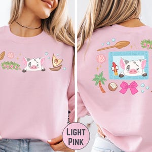 A woman wearing a pink long-sleeved shirt with a cartoon pig design and various other colorful illustrations on the back.