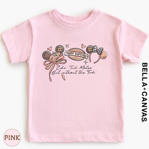 A pink t-shirt with a graphic design featuring a character and the text "Tow Mater" along with the phrase "Like Tum Mater But without the Tui".