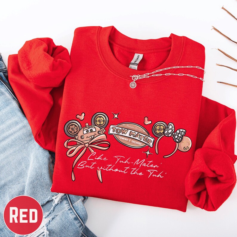 A red sweatshirt with a cartoon character design and text printed on it, along with a necklace and a pair of jeans.
