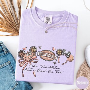 a purple t-shirt with a cartoon character design, a necklace, and some other clothing items such as jeans and a sweater.