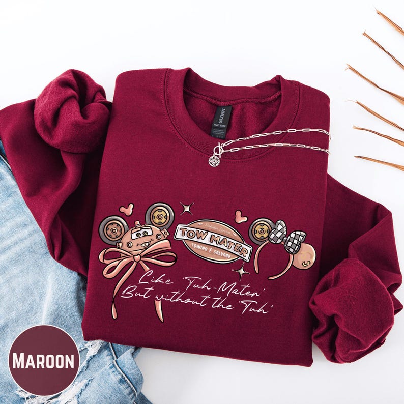 A maroon sweatshirt with a graphic design and text printed on it, along with a necklace and some other clothing items.