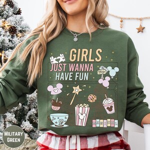 A woman wearing a green sweatshirt with a graphic design featuring various Disney-themed items and text.