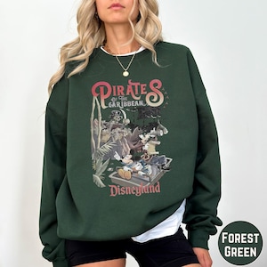 A woman wearing a green sweatshirt with a graphic of Disney characters from the Pirates of the Caribbean ride at Disneyland.
