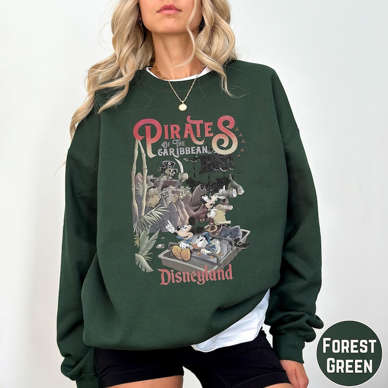 A woman wearing a green sweatshirt with a graphic of Disney characters from the Pirates of the Caribbean ride at Disneyland.