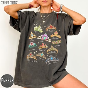 A person wearing a black t-shirt with a graphic design of various crowns and tiaras printed on it.