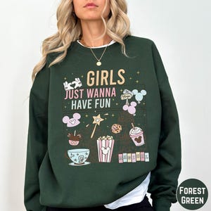 A woman wearing a green sweatshirt with a graphic design featuring various Disney-themed items and text.