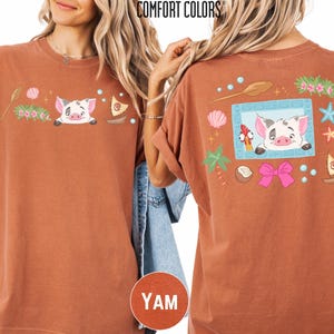 a woman wearing a brown t-shirt with a cartoon pig design and various colorful elements, such as flowers, stars, and a bow.
