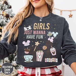 A woman wearing a gray sweatshirt with a graphic design featuring various Disney-themed items and text.