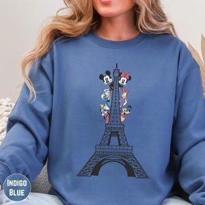 A woman wearing a blue sweatshirt with a graphic of the Eiffel Tower and Disney characters on it.